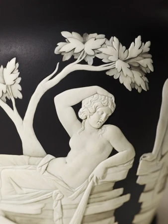Close-up of a bas-relief sculpture on a black vase featuring a reclining nude woman under a tree. Classic art inspiration.