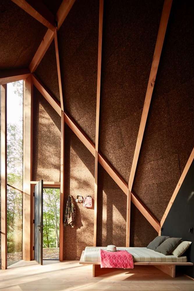 Cozy interior of a wooden cabin featuring a daybed, minimalist decor, and views of the surrounding nature through a large window.