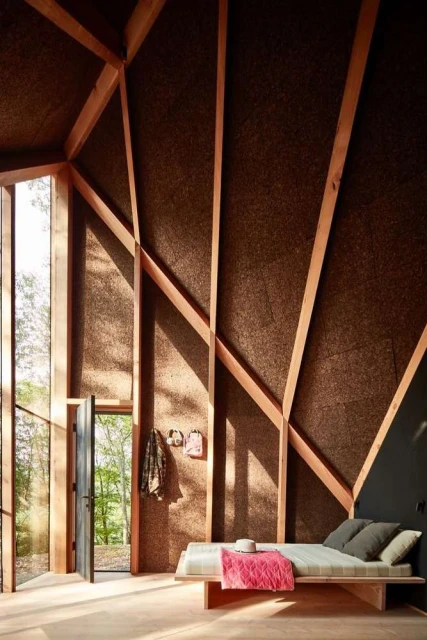 Cozy interior of a wooden cabin featuring a daybed, minimalist decor, and views of the surrounding nature through a large window.