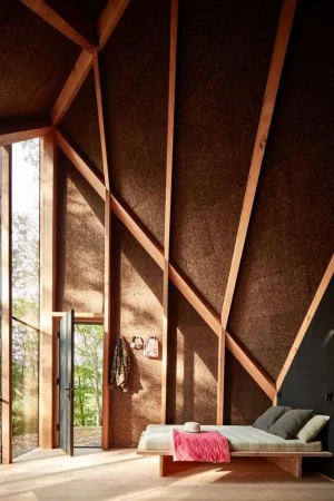Cozy interior of a wooden cabin featuring a daybed, minimalist decor, and views of the surrounding nature through a large window.