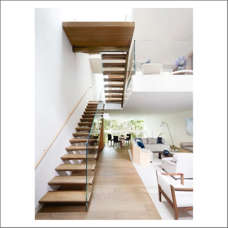 Open-plan house interior featuring a floating staircase with wood treads, glass railings, a dining set, and a living area with white sofas.