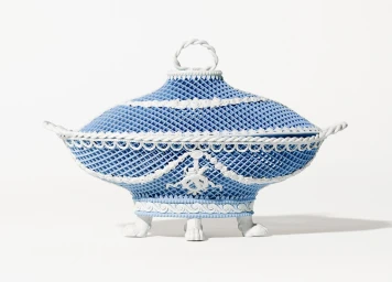 Ornate blue and white ceramic tureen with a pierced lattice pattern, twisted handles, and paw feet against a white background.
