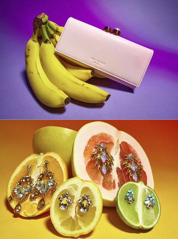 Still life flat lay of bananas with a pink Ted Baker wallet and cut citrus fruit with earrings on a yellow and purple background.