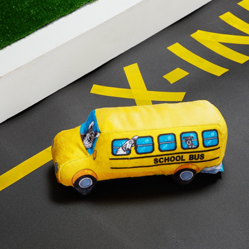 Close-up of a yellow school bus plush toy on a grey surface with yellow markings, suggesting a road, under bright, natural light.