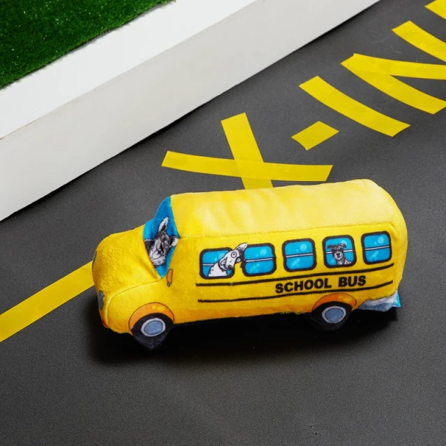 Close-up of a yellow school bus plush toy on a grey surface with yellow markings, suggesting a road, under bright, natural light.
