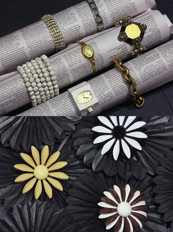 Close-up of a variety of jewelry including bracelets, watches, and brooches, arranged on newspaper rolls and a black floral surface.