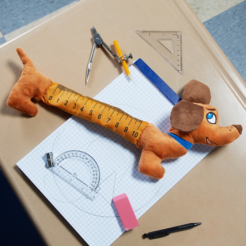 Overhead shot of dachshund plush toy doubling as a measuring tape, surrounded by geometric tools and placed on a desk.