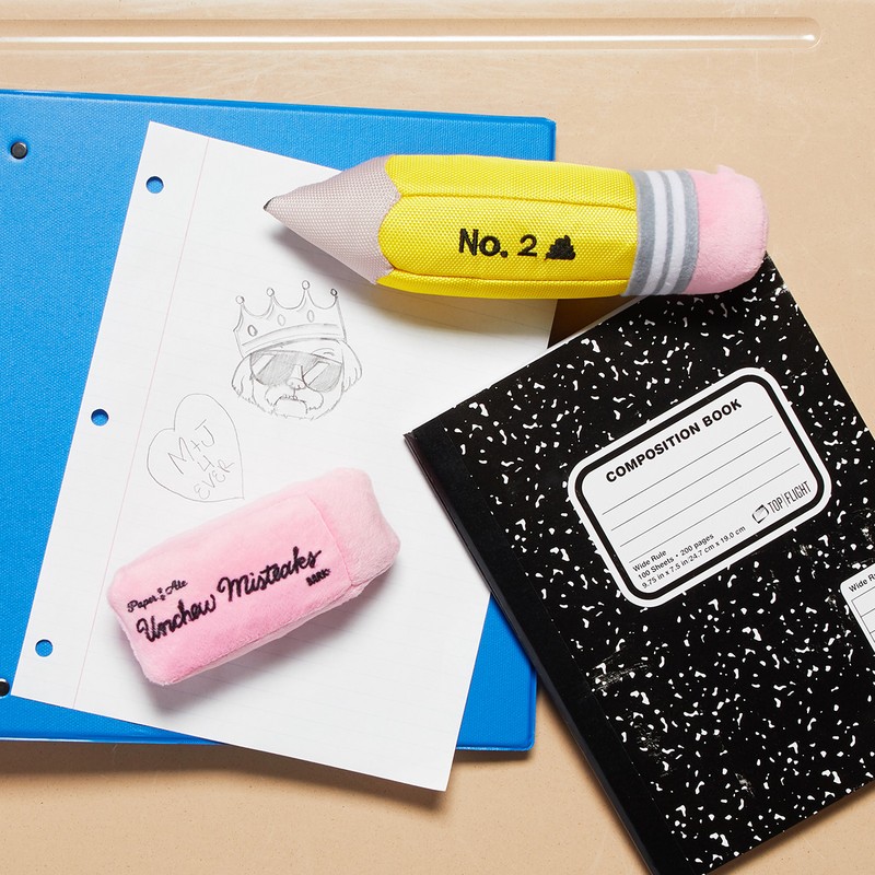 Still life of school supplies: a composition notebook, pencil-shaped pencil case, eraser, binder, and paper with a doodle on a desk.