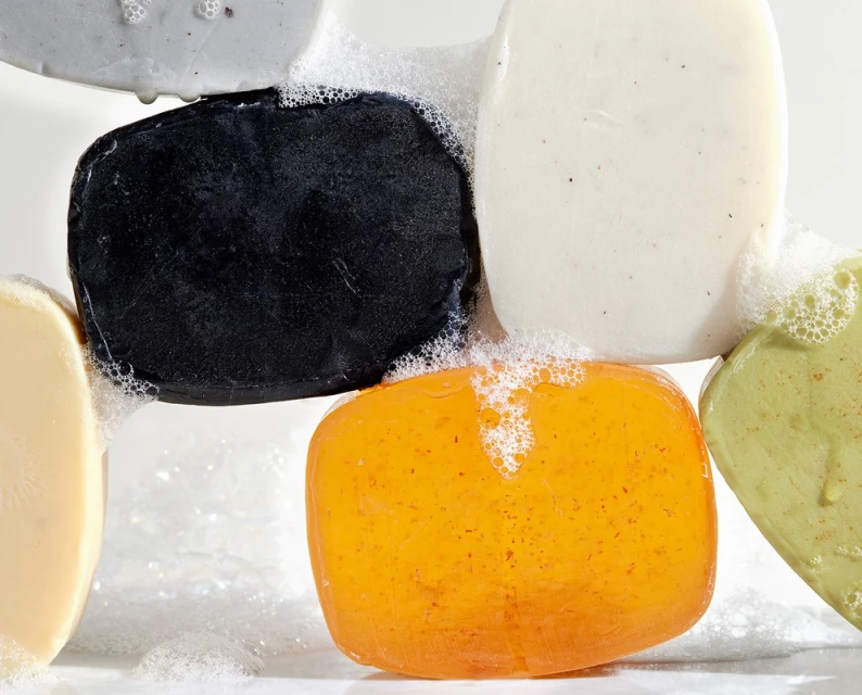 Close-up of assorted bars of multicolored soap with white bubbles on a white background. Beauty and personal care product.