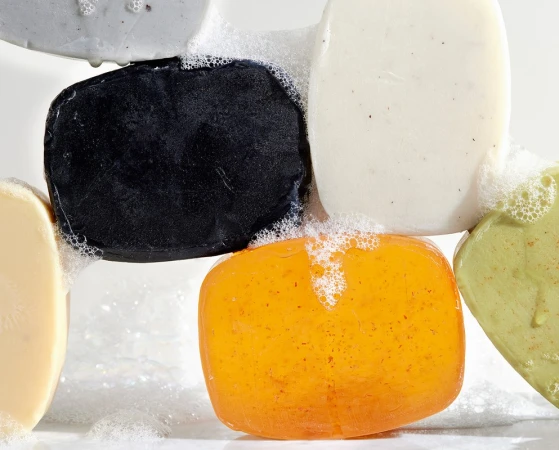 Close-up of assorted bars of multicolored soap with white bubbles on a white background. Beauty and personal care product.