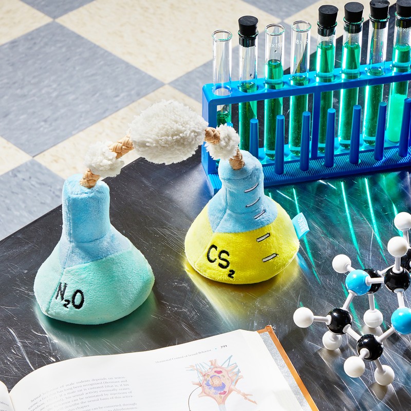 Two plush toy chemistry beakers connected, scientific equipment, test tubes, and a textbook create a playful science scene.
