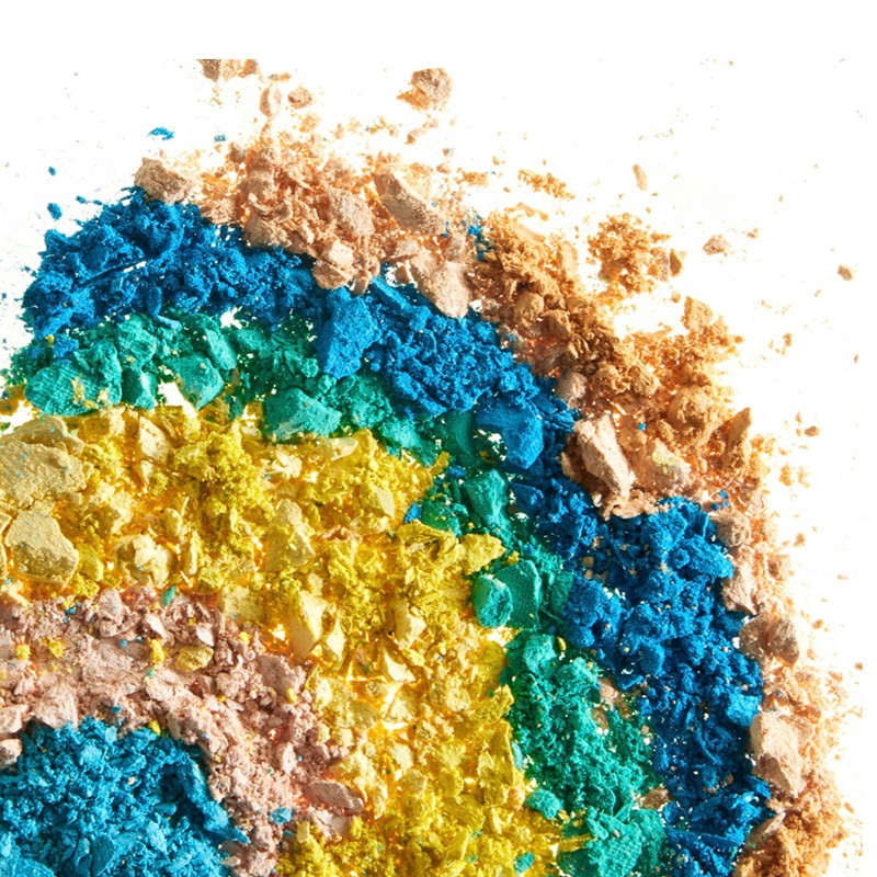 Close-up of vibrant cosmetic powder in shades of yellow, green, blue, and bronze against a bright white background. Beauty concept.