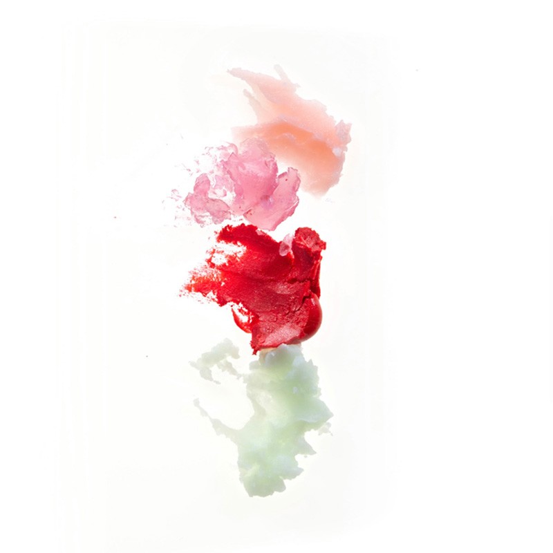 Close-up of a vertical column of lipstick smears in peach, pink, and red on a white background, with a partial reflection.