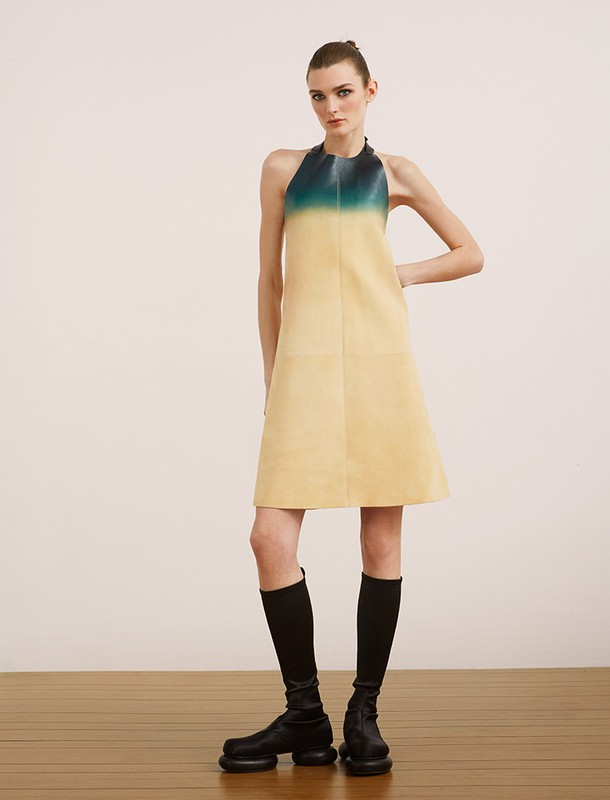 A slender female model showcases a halter dress in gradient yellow and teal, paired with knee-high socks and chunky black boots in a studio.