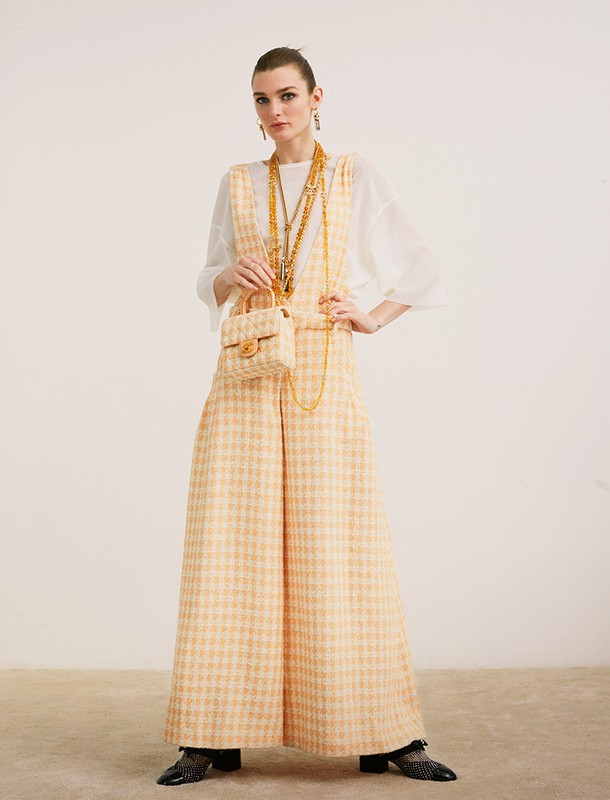 Model in yellow tweed overalls over a white top holding a matching handbag styled by Thomas Tomczak against a plain backdrop