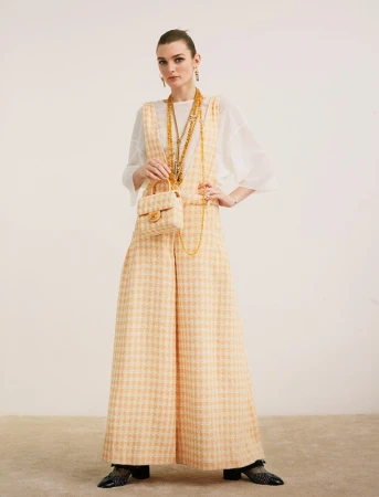 Model in yellow tweed overalls over a white top holding a matching handbag styled by Thomas Tomczak against a plain backdrop