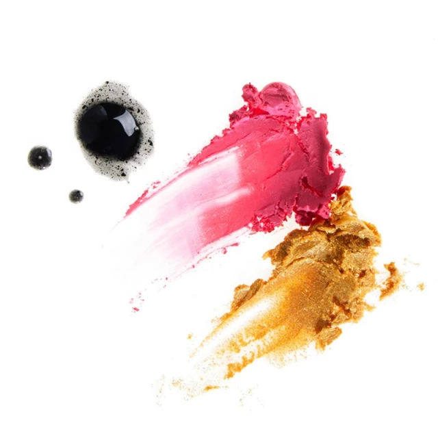 A swatch of gold, pink, and black cosmetics swiped on a white surface, showcasing textures and makeup for beauty content.