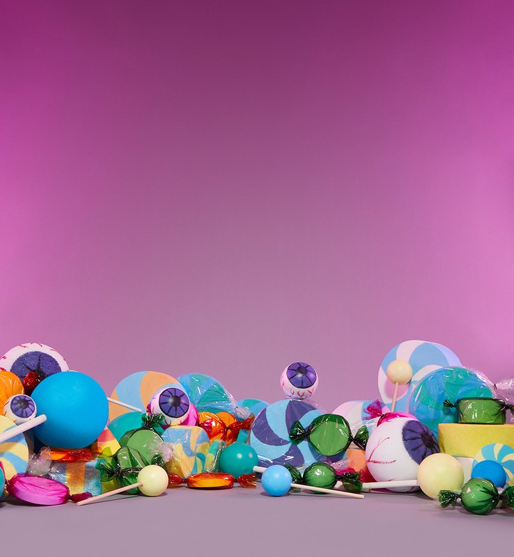 Still life of assorted Halloween candy including wrapped lollipops and gumballs, displayed against a pink to purple gradient background.