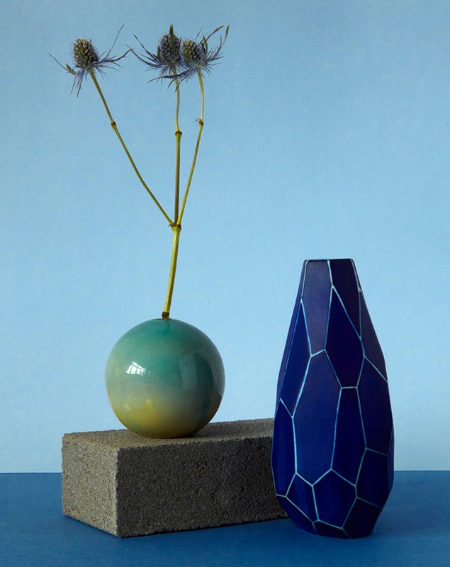 Still life of two vases, one round with blue to yellow gradient holding thistle, and a geometric patterned blue vase.