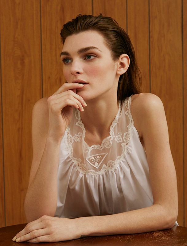 Portrait of a woman wearing a white top with lace trim. The background features wood panelling and a polished brown table.