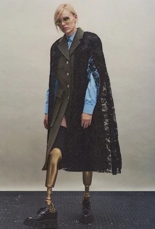 Fashionable woman in a lace cape, stylish top, and metallic prosthetic legs poses against a neutral background, showcasing unique style.