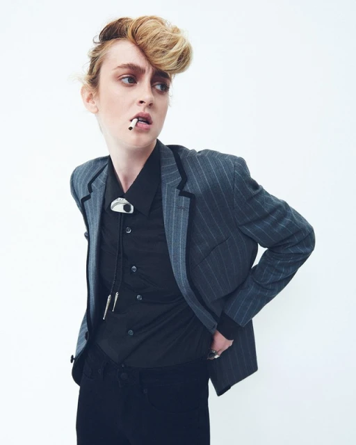 Stylish young adult woman in a pinstripe blazer poses with a cigarette against a white background in a fashion editorial shot.