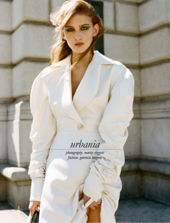 Model in a white puffed-sleeve coat with green eyeshadow standing in front of neoclassical stone columns