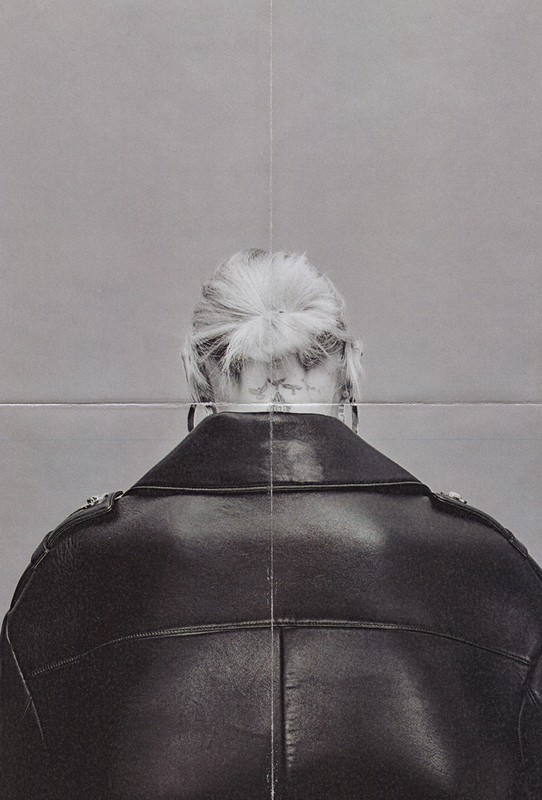 Monochrome studio shot of an adult wearing a black leather jacket, seen from the back, with a neutral grey backdrop.