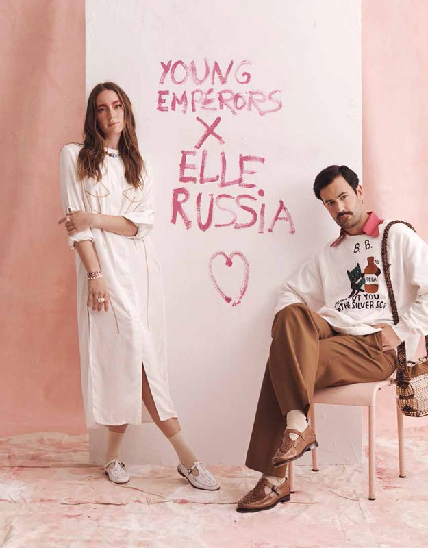 A fashion shot with a young adult female in a white dress and a young adult male in a sweatshirt and brown pants near a wall.