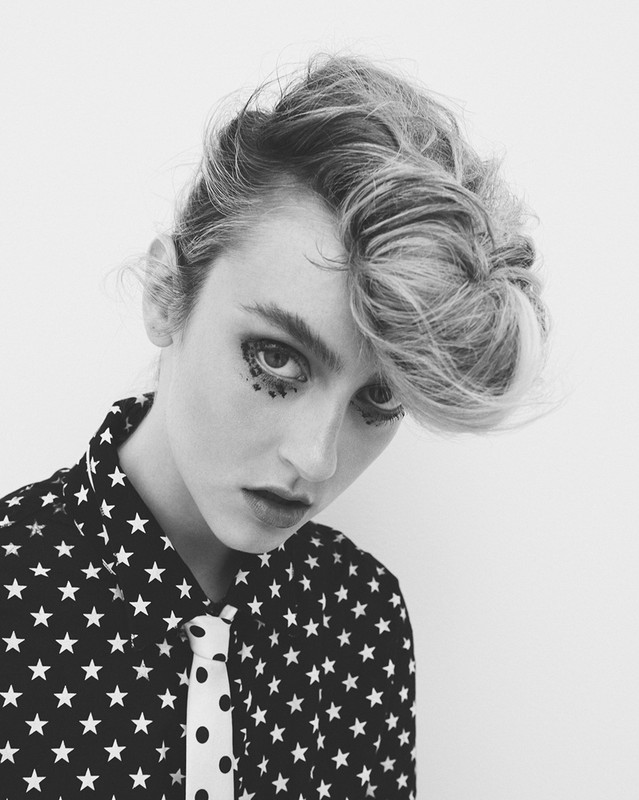 Black and white portrait of a stylish adult female model with glitter eye makeup, wearing a star-patterned shirt and polka dot tie.