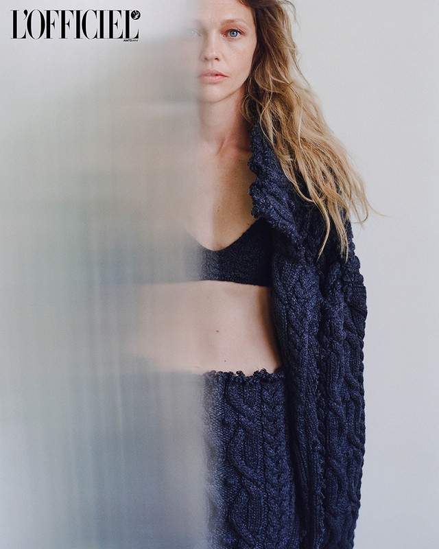 Woman wearing knitted navy blue co-ord set and bra top posing in front of a white wall with L'Officiel magazine logo.