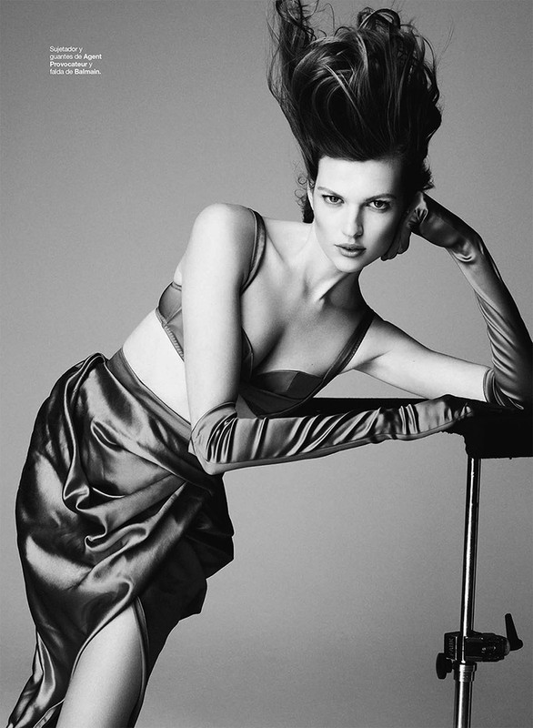 Monochrome fashion shot of a woman in a bra and draped skirt, posing in a studio with dramatic hair and long gloves. 