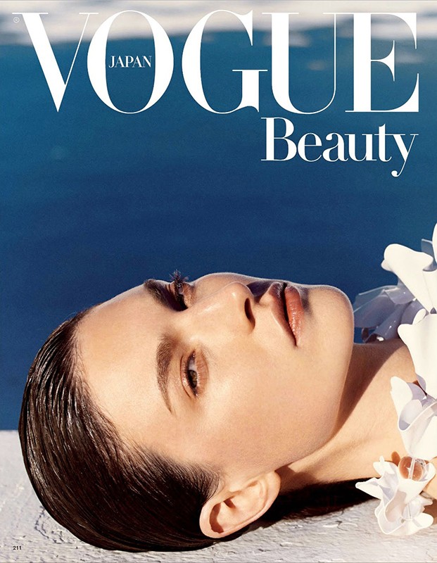 Close-up of an adult female model with wet hair lying near the water, featured on a Vogue Japan beauty magazine cover.