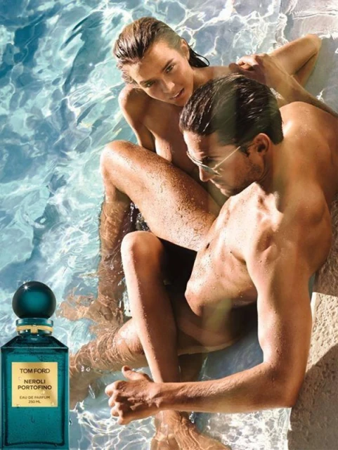 Fragrance ad in a pool featuring a man with glasses embracing a woman in the water with a perfume bottle in the foreground.