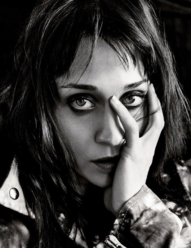 Black and white portrait of an adult female with long dark hair, looking directly at the camera with her hand near her face.