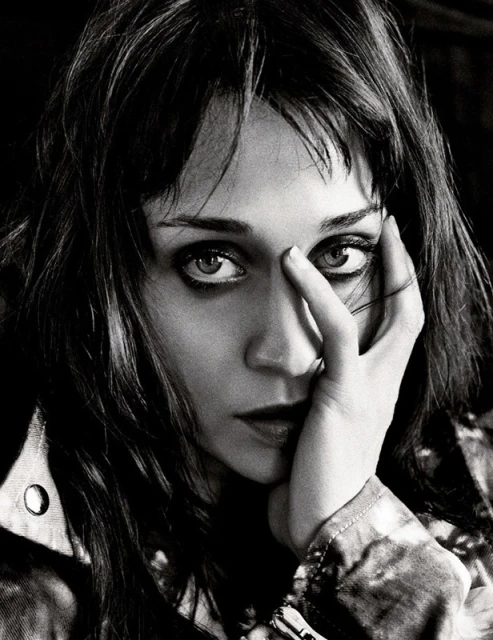 Black and white portrait of an adult female with long dark hair, looking directly at the camera with her hand near her face.