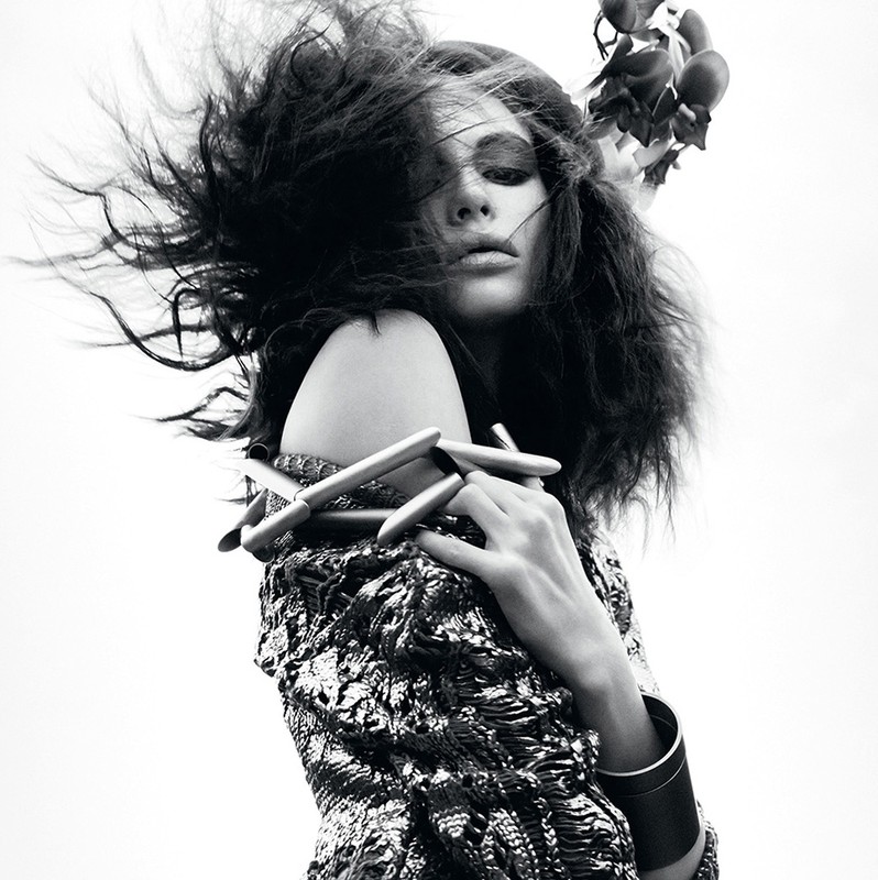 Artistic black and white close-up of a woman with dramatic hair and floral headpiece, showcasing textured clothing and jewelry.