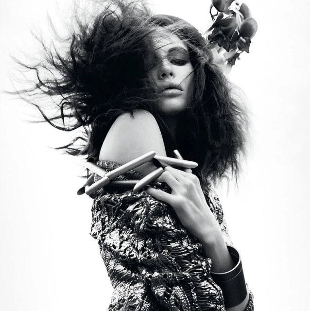 Artistic black and white close-up of a woman with dramatic hair and floral headpiece, showcasing textured clothing and jewelry.