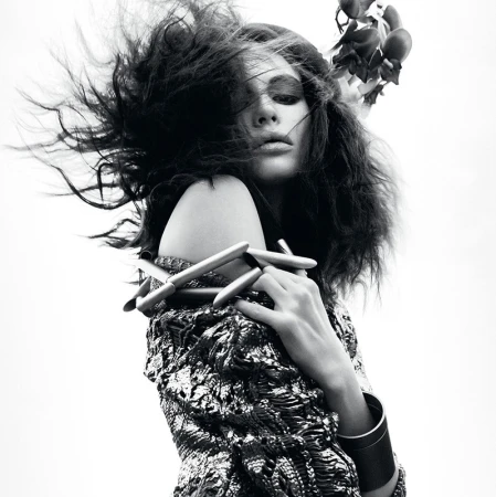 Artistic black and white close-up of a woman with dramatic hair and floral headpiece, showcasing textured clothing and jewelry.