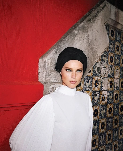 Close-up of a woman in a white top and black headscarf poses against a colorful tiled wall and red accent wall, beauty concept.