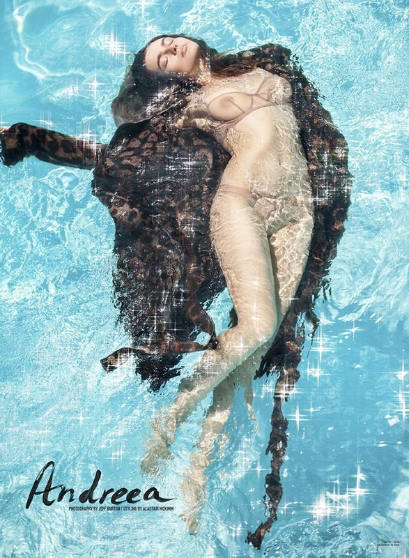 Woman floating on her back in a sparkling blue swimming pool wearing a dark leopard print coat