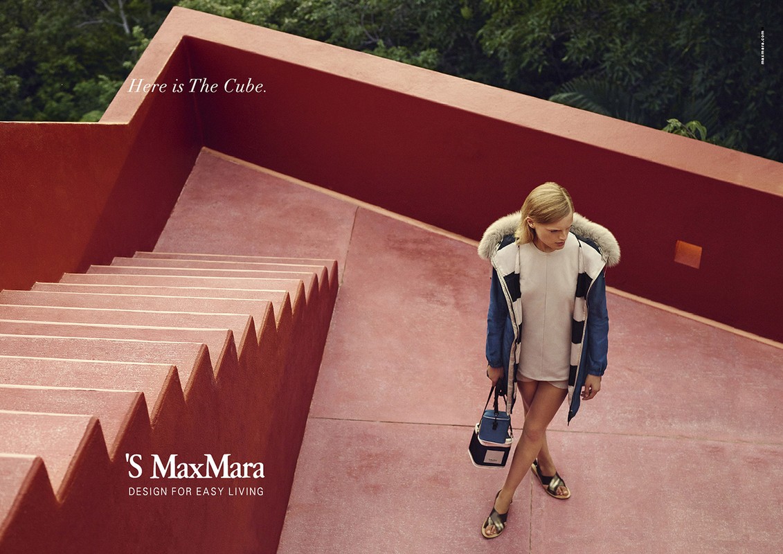 Fashion shot of an adult woman walking down coral-colored outdoor steps, wearing a jacket, shorts, and sandals with a purse.