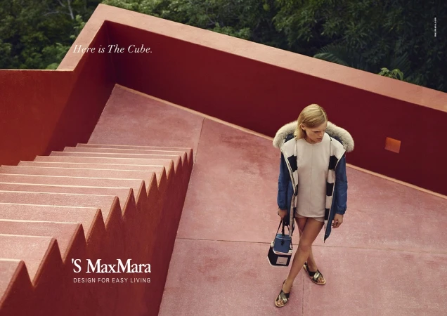 Fashion shot of an adult woman walking down coral-colored outdoor steps, wearing a jacket, shorts, and sandals with a purse.