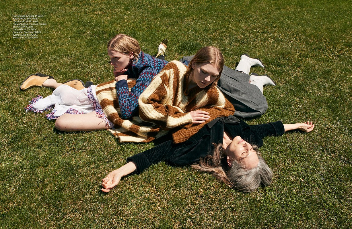 Three female models lying on a green grass lawn outdoors, featuring patterned sweaters and textured styling.