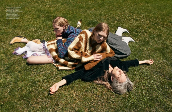 Three female models lying on a green grass lawn outdoors, featuring patterned sweaters and textured styling.