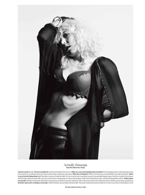 Black and white portrait of a woman with curly blonde hair wearing a bra and robe, posing indoors against a white background.