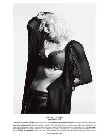 Black and white portrait of a woman with curly blonde hair wearing a bra and robe, posing indoors against a white background.