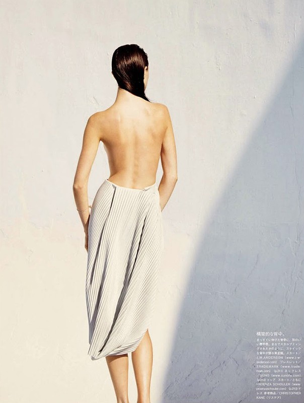 Back view of an adult woman with brown hair in an elegant ivory-colored skirt against a neutral studio backdrop, bathed in soft light.