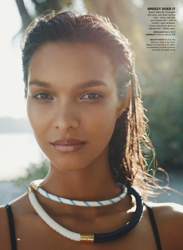 Close-up portrait of a tanned woman with wet hair and rope necklaces on a beach with blurred background and sunlight.
