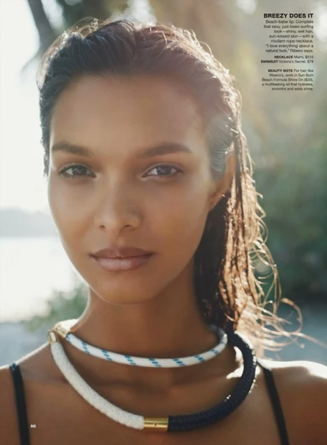 Close-up portrait of a tanned woman with wet hair and rope necklaces on a beach with blurred background and sunlight.
